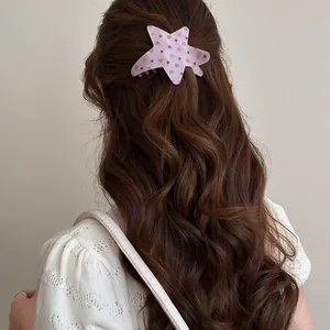 Back view of a pink polka dot star-shaped acetate hair clip on wavy brown hair