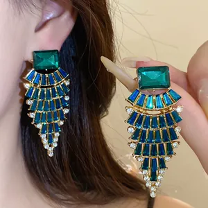 Détail de boucles d'oreilles en éventail exagérées avec des cristaux verts et bleus