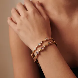 Detailansicht eleganter goldener Wellenarmreifen mit bunten ovalen Zirkonia am Handgelenk