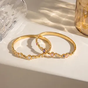 Nahaufnahme von goldenen Edelstahlarmbändern mit bunten ovalen Zirkonia-Steinen