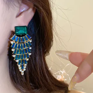 Gros plan de boucles d'oreilles exagérées en éventail émeraude et bleu avec strass.