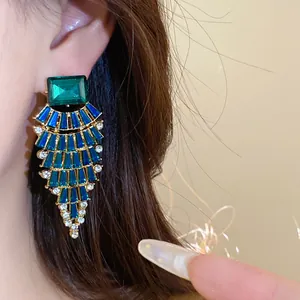 Gros plan de boucles d'oreilles en éventail avec des strass bleus et verts brillants.