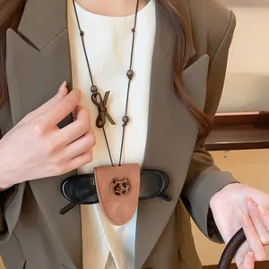 Detail of a brown leather eyeglass holder necklace featuring a leopard cat charm on model