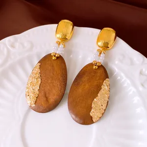 Close-up of vintage oval wooden drop earrings with gold leaf and pearls detail.