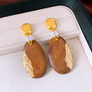 Macro detail of elegant wooden oval pendant earrings with gold foil and white pearls