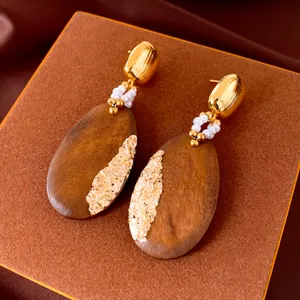 Close-up detail of retro oval wood drop earrings with gold leaf and pearl accents