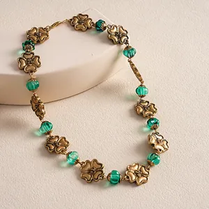 Detail view of a vintage-style metal flower necklace with green resin beads on a display.