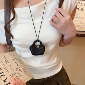 Close-up of a stylish black woven bag pendant necklace worn by a model on a white top