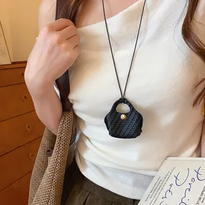 Model wearing a woven mini bag pendant necklace over a white top and brown skirt