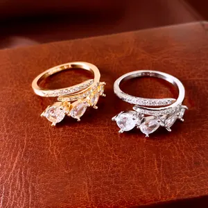 Detailed close-up showing gold and silver zircon teardrop open rings on brown leather.