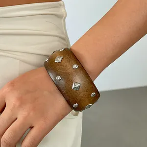 Detailed view of a vintage wooden bangle featuring geometric silver metal studs on wrist