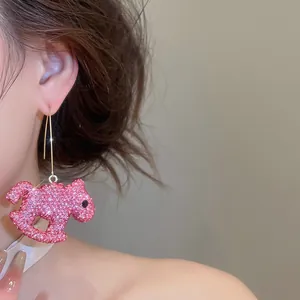 Détail de boucles d'oreilles pendantes en forme de cheval à bascule serties de cristaux roses