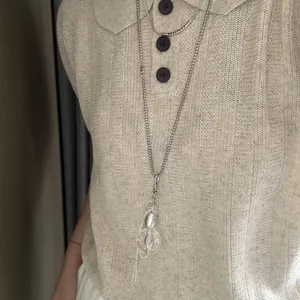 Detailansicht einer langen silbernen Kette mit klarem Anhänger über einer Strickweste