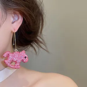 Vue rapprochée d'une boucle d'oreille cheval à bascule en strass roses sur l'oreille