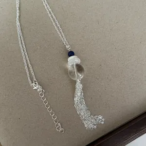 Detail einer Halskette mit Quastenanhänger, klaren und blauen Perlen auf einer Silberkette.