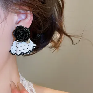 Close-up of black flower stud earring with a white polka-dot ruffle skirt detail.