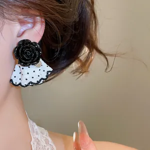 Elegant black rose stud earrings with white polka dot skirt drop detail on model.