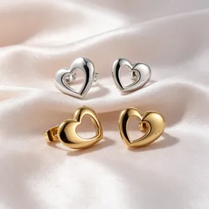 Detail shot of polished gold and silver hollow heart stud earrings on soft cream silk fabric