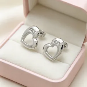 Macro view of silver hollow heart-shaped stud earrings with inlaid stones in pink box