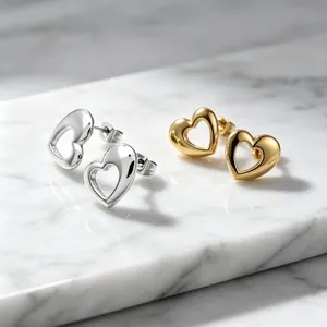 Close-up of gold and silver titanium steel hollow heart-shaped stud earrings on marble