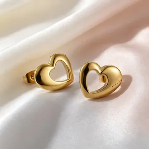 Detailed macro view of gold-tone hollow heart-shaped stud earrings on white satin fabric