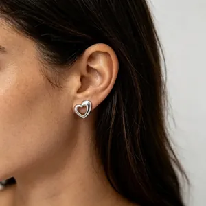 Close-up shot of minimalist silver hollow heart stud earrings worn on an ear for a daily look