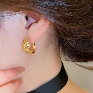 Detailweergave van elegante gouden oorringen met geometrische textuur en zirkoon