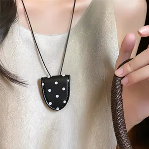 Detail view of a black leather polka dot glasses holder necklace worn on a satin top.