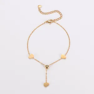 Detail van een gouden roestvrijstalen armband met hartbedeltjes en een kwastje.