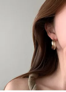 Vista laterale dettagliata di eleganti orecchini a cerchio dorati a costine indossati da modella
