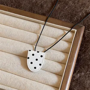 Close-up detail of a minimalist leather polka dot pendant necklace on a jewelry tray