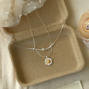 Dettaglio della collana a doppio strato con ciondolo a margherita e piccole perle.
