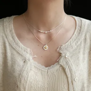Dettaglio di una collana a strati con margherita e perle indossata sul collo