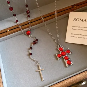 Détail du pendentif croix en résine rouge et du collier de perles dans sa boîte