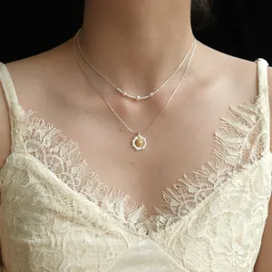 Dettaglio di una collana con ciondolo a fiore stratificata con perle su modella