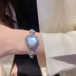 Close-up detail showing the silver heart-shaped diamond bracelet watch worn on a woman's wrist.