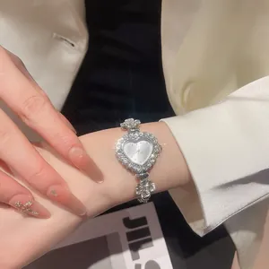 Detailed close-up of a heart-shaped diamond watch with a floral link bracelet on a wrist