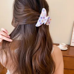 Detalle de una pinza para el pelo de acrílico floral en cabello largo ondulado de color castaño.