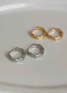 Minimalistische gedrehte Creolen in Gold- und Silbertönen auf einer weißen Oberfläche.