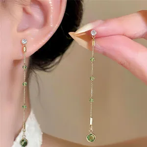 Detailed view of elegant gold tassel earrings featuring sparkling green and clear zircons.