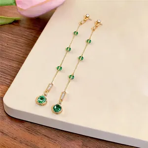 Detail shot of elegant long tassel earrings with green zircon stones on a cream surface.