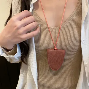 Vue détaillée d'un collier porte-lunettes en cuir rose porté sur un haut côtelé beige.