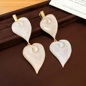 Macro detail shot of vintage white heart-shaped enamel drop earrings with gold framing.