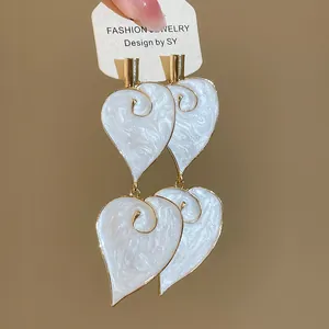 Detailed shot of vintage white enamel heart leaf earrings with gold spiral pattern
