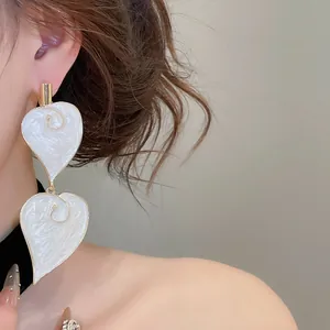 Close-up of elegant vintage white drip oil heart-shaped dangle earrings on model.