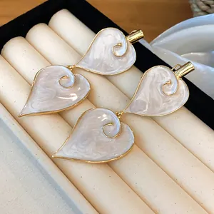 Close-up of vintage heart-shaped enamel dangle earrings in elegant cream and gold