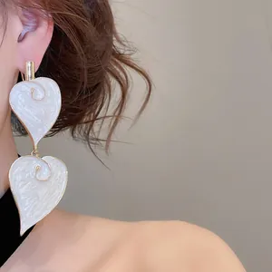 Detailed view of vintage white drip oil leaf-shaped pendant earrings on model.