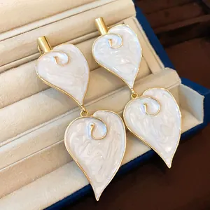 Close-up of vintage heart leaf dangle earrings with white enamel and gold finish