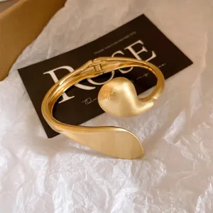 Close-up detail of a gold sculptural twisted bracelet featuring a unique matte brushed metal finish