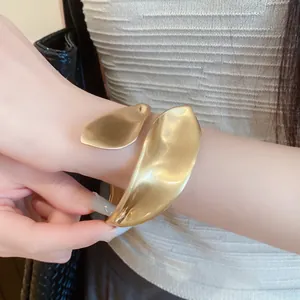 Close-up detail of a large gold-toned sculptural wrap bracelet worn on wrist